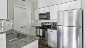 A kitchen with white cabinets, a stainless steel refrigerator, a microwave, a stove, and a sink. - Landing | Modern 1BD in Copperfield (Cypress)