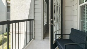 A balcony with a black metal railing, a black cushioned bench, and a door with a window. - Landing | Beautiful 1BD in Copperfield (Cypress)