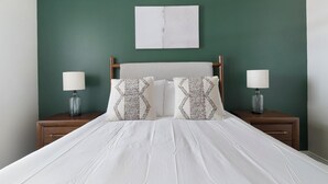 Een bed met wit beddengoed, twee nachtkastjes met lampen en een groene wand.