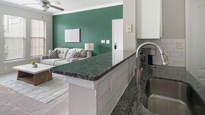 A modern kitchen with a granite countertop, stainless steel sink, and a ceiling fan. - Landing | Stylish 1BD in Copperfield (Cypress)