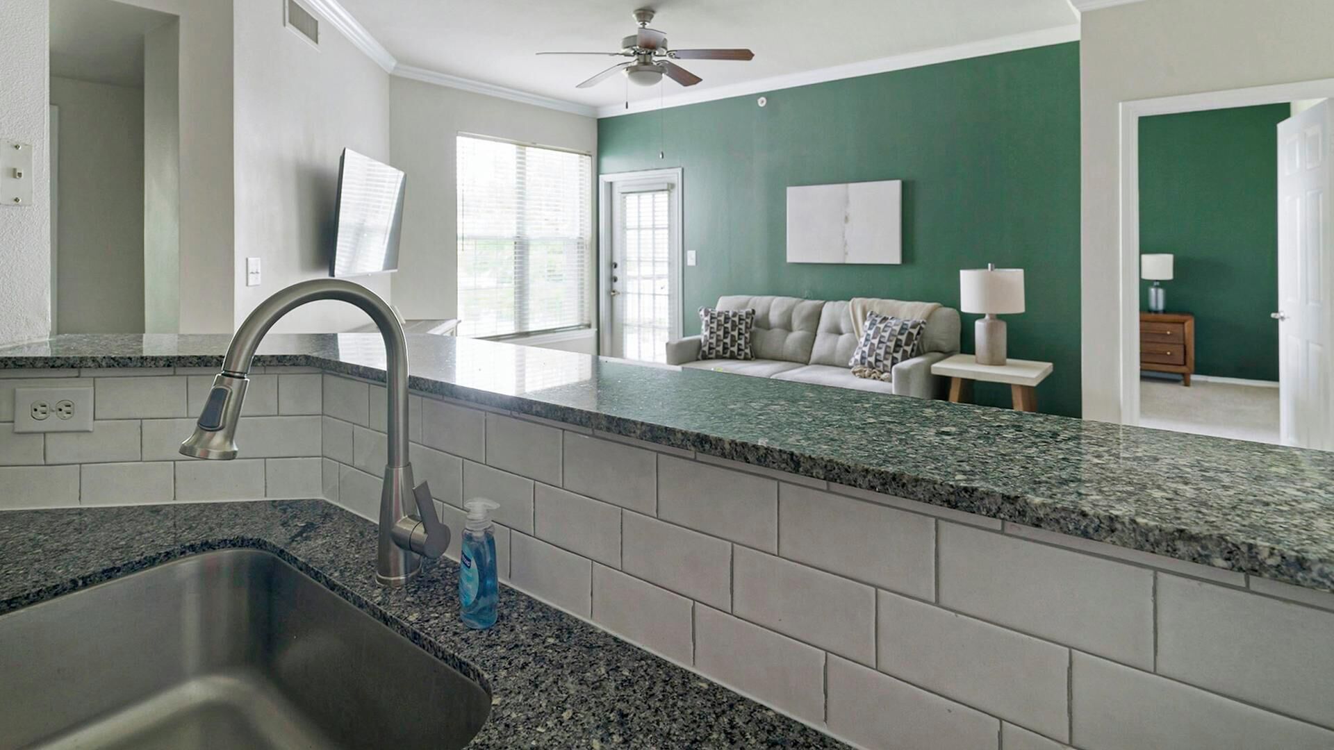 A kitchen with a granite countertop, stainless steel sink, and a ceiling fan.