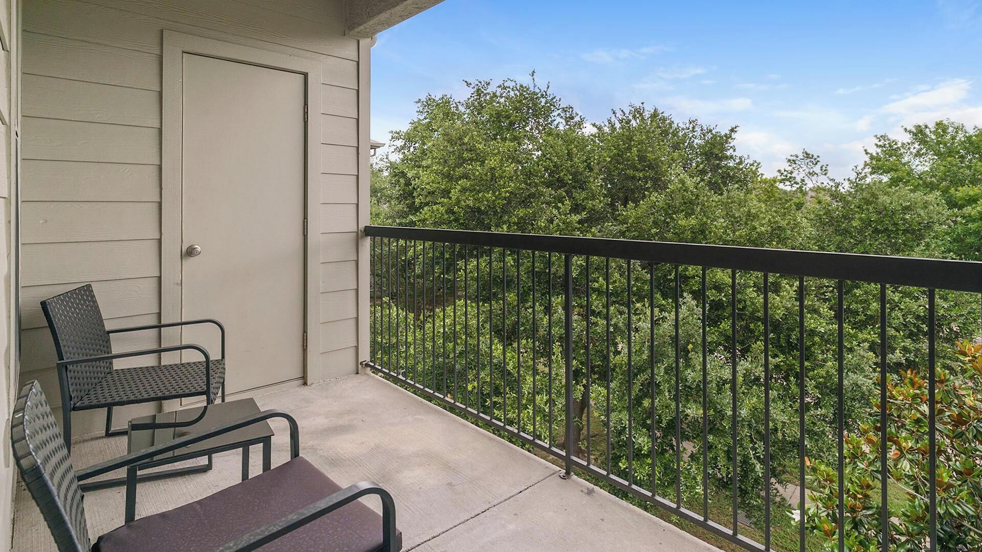 Un balcon avec une rambarde en métal, une porte et deux chaises.