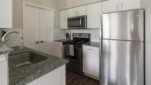 A kitchen with white cabinets, a stainless steel refrigerator, a microwave, a stove, and a sink. - Landing | Stylish 1BD in Copperfield (Cypress)