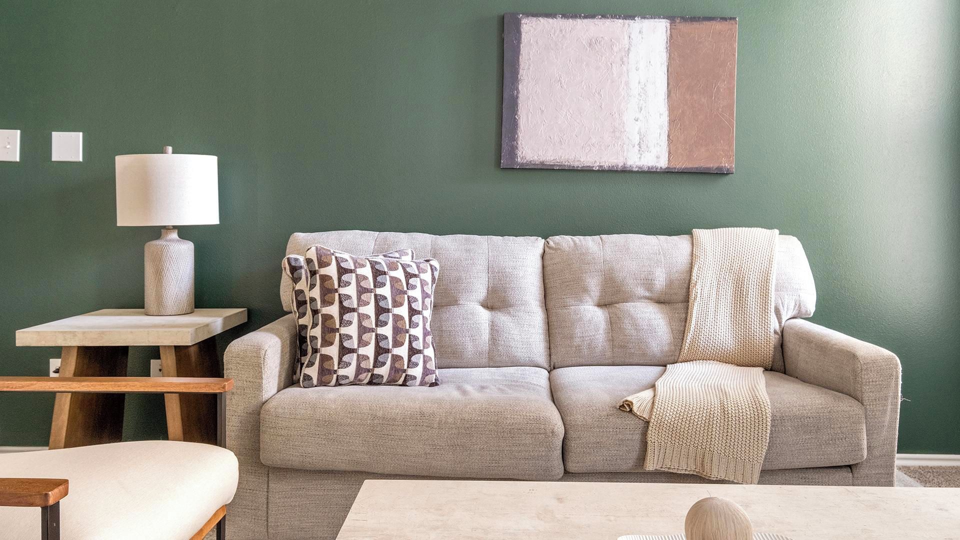 Un salon avec un canapé, une table d’appoint avec une lampe et un tableau accroché au mur.