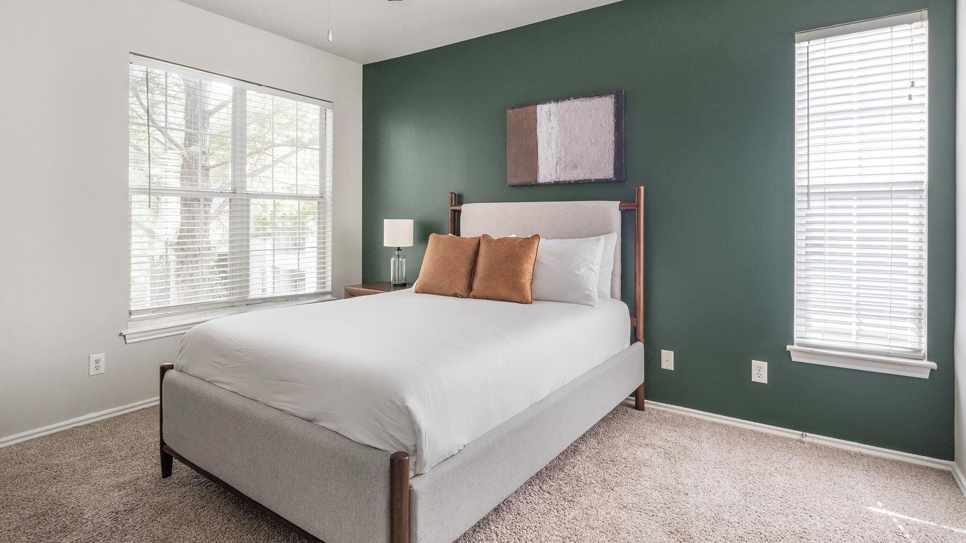 A bedroom with a bed, two bedside tables, a nightstand, and a window with blinds.