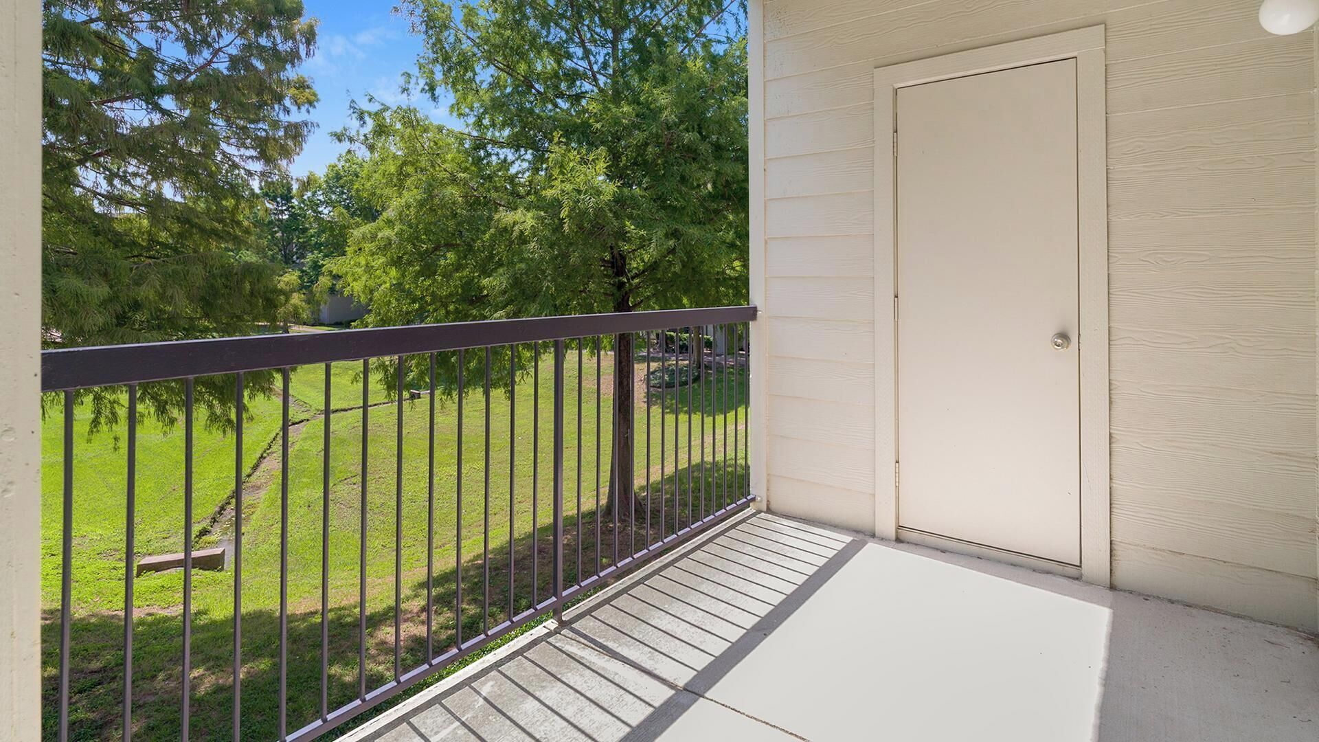 Un balcon doté d’une rambarde en métal, d’une porte et offrant une vue sur un espace verdoyant avec des arbres.