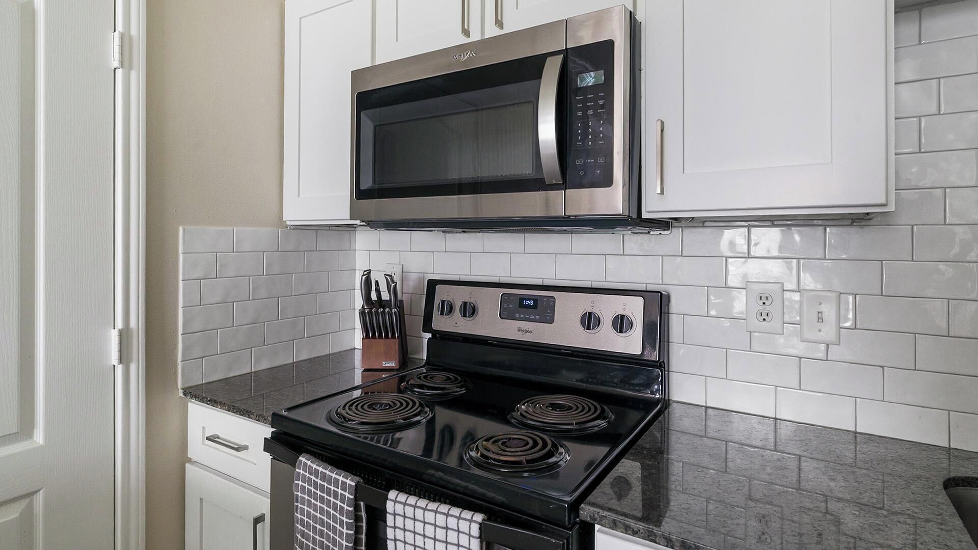 A kitchen with a microwave, stove, and knife block.