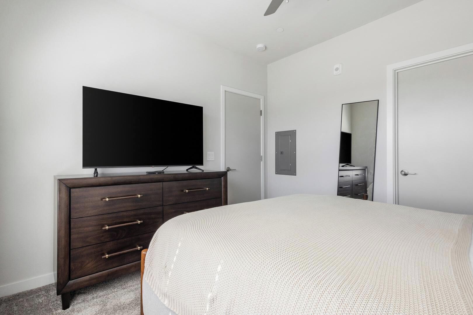 Een slaapkamer met een bed, een dressoir, een televisie en een deur.