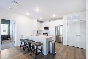 A modern kitchen with a central island, bar stools, stainless steel appliances, and a trash can.