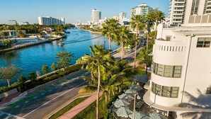 A waterfront hotel with a curved road, palm trees, and a river. - King | Hotel Trouvail | Boutique Secret, Beach Block, Faena District (Miami Beach)