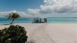A beach with a palm tree, a small gazebo, and a boat dock. - Tranquil 4-bedroom 3-bath house with 50' boat dock in delightful Treasure Cay (Treasure Cay)