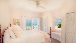 A bedroom with a bed, a ceiling fan, a window with a view of the sea, and a door with shutters. - Tranquil 4-bedroom 3-bath house with 50' boat dock in delightful Treasure Cay (Treasure Cay)