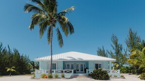 A beachfront property with a white building, a palm tree, and a stone pathway leading to the entrance. - Tranquil 4-bedroom 3-bath house with 50' boat dock in delightful Treasure Cay (Treasure Cay)