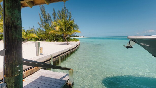 A wooden pier extending into clear turquoise waters, surrounded by palm trees and a boat docked nearby. - Tranquil 4-bedroom 3-bath house with 50' boat dock in delightful Treasure Cay (Treasure Cay)