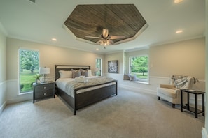 A bedroom with a large bed, a ceiling fan, a nightstand, a chair, and large windows. - Pool, Theater, Game Room + Massive Private Lawn (Frisco)