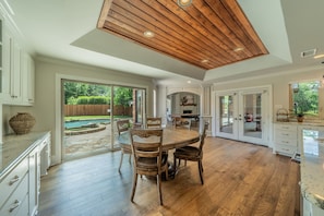A spacious kitchen with wooden flooring, a dining area with a round table, and a view of a backyard with a swimming pool. - Pool, Theater, Game Room + Massive Private Lawn (Frisco)