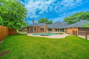 A residential property with a brick house, a swimming pool, and a fenced yard.