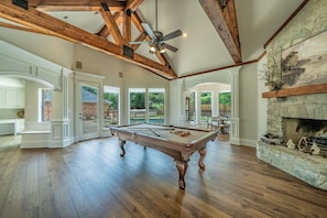A spacious room with a pool table, a stone fireplace, and a ceiling fan.