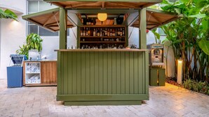 Un espace bar extérieur verdoyant, avec des étagères remplies de bouteilles et de verres, un comptoir en bois et des plantes en pot.