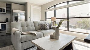 Een moderne woonkamer met een bank, een salontafel en uitzicht op de straat door grote ramen.