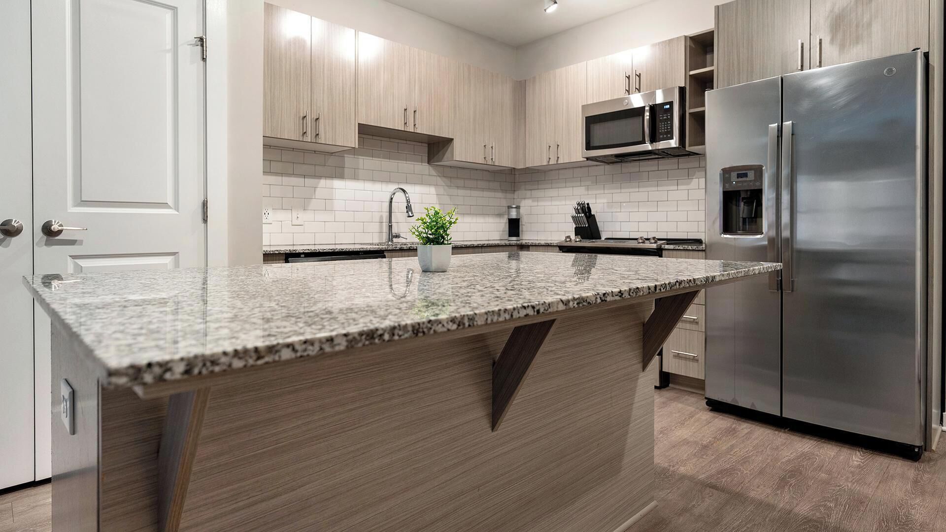 A modern kitchen with a granite countertop, stainless steel appliances, and light wood cabinetry.