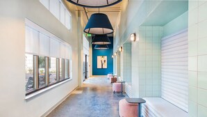 Een gang met een blauwe wand, een plafondlamp en een bankje.