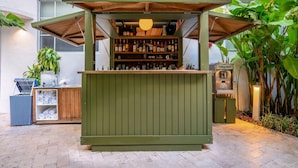 Un espace bar extérieur verdoyant, avec des étagères remplies de bouteilles et de verres, un comptoir en bois et des plantes en pot.
