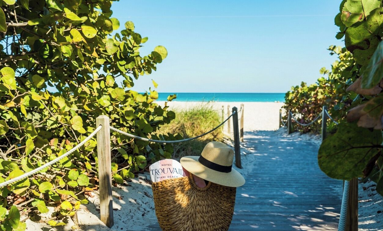 Ein Strandweg führt zu einem Hotel namens 'TROUVAULT' mit einem Schild, das angibt, dass es sich in Miami Beach befindet.