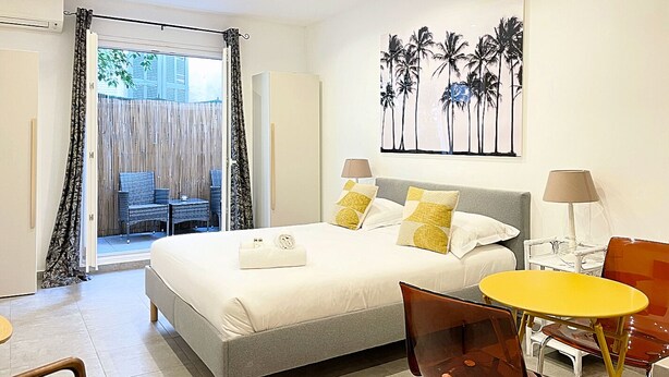 A hotel room with a bed, a small table, a chair, a balcony with a view, and a painting on the wall. - Viva Riviera Charming Studio with Terrace (Cannes)