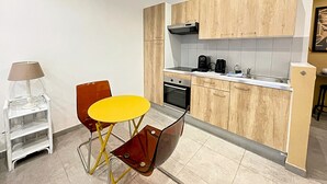 A compact kitchen with wooden cabinets, a small dining table, and a coffee maker. - Viva Riviera Charming Studio with Terrace (Cannes)