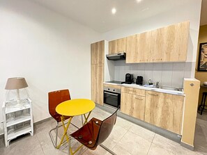 A compact kitchen with wooden cabinets, a small dining table, and a coffee maker. - Viva Riviera Charming Studio with Terrace (Cannes)