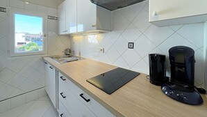A modern kitchen with white cabinets, a window with a city view, a coffee maker, and a tablet on the counter. - Viva Riviera Apartment with balcony near the sea (Cannes)