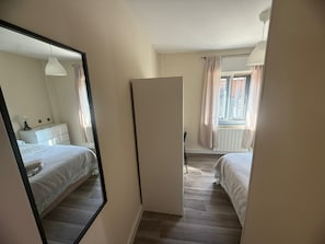 Ett sovrum med en stor spegel, två sängar, en byrå och ett fönster med gardiner.