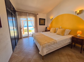 A bedroom with a bed, a nightstand, a lamp, a picture on the wall, and a view of the ocean through the window. - Villa dame de Salema with magnificent ocean view and heated pool (Salema8650-)