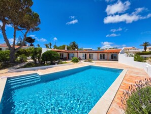 A swimming pool with a tiled deck, surrounded by greenery and a building with a tiled roof. - Villa dame de Salema with magnificent ocean view and heated pool (Salema8650-)