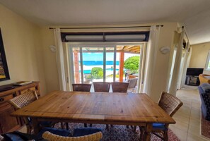 Un coin repas avec une table en bois et des chaises en osier, un téléviseur et une vue sur l’océan.