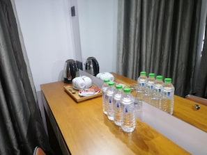 Una habitación de hotel con una mesa de madera, una tetera, una cafetera y varias botellas de agua.