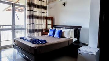 A hotel room with a bed, a small desk, a refrigerator, a window with curtains, and a balcony.