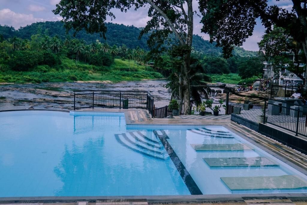 A swimming pool with a surrounding deck, a fence, and a view of a natural landscape with trees and hills.