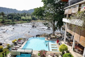 A pool with a view of a river and surrounding greenery, a covered outdoor seating area, and a building with a balcony. - The Elephant Bay - Pinnawala (Rambukkana)