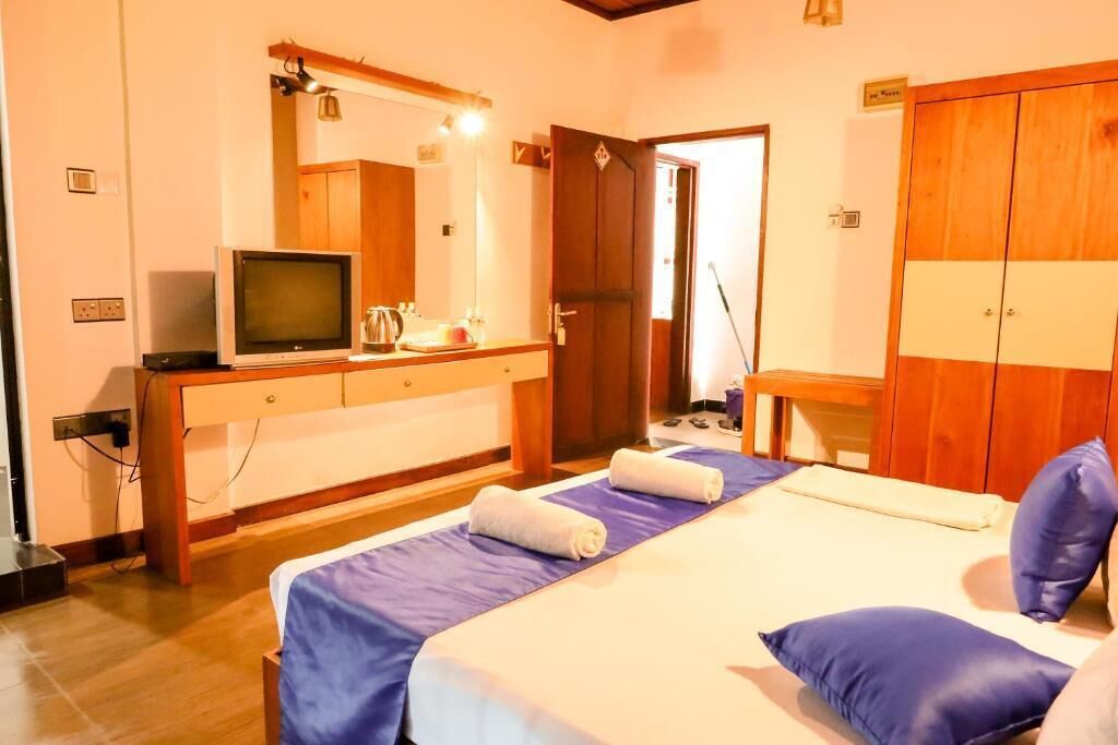 A hotel room with a bed, a TV, a wooden wardrobe, and a bathroom area.