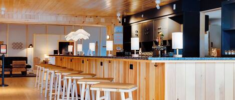 Una zona de bar con taburetes de madera, una barra y una lámpara colgante.