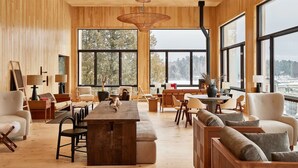 A spacious room with wooden walls, large windows, a central wooden table, and multiple seating areas. - Laurel | 2 Queen | Olympic History, Mirror Lake, On-Site Restaurant (Essex County)