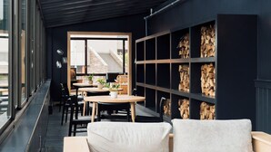 A modern interior with a long bench, tables, chairs, and a wall with stacked firewood. - Laurel | 2 Queen | Olympic History, Mirror Lake, On-Site Restaurant (Essex County)
