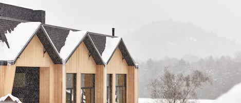 Un bâtiment moderne en bois, doté d’un toit en pente, de grandes fenêtres et surplombant un paysage enneigé.