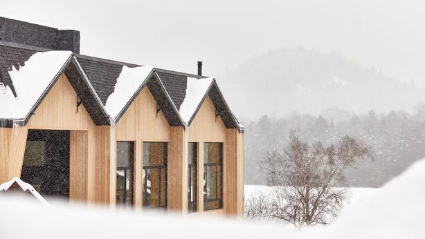 Un edificio moderno de madera con techo inclinado, ventanas grandes y un paisaje nevado.