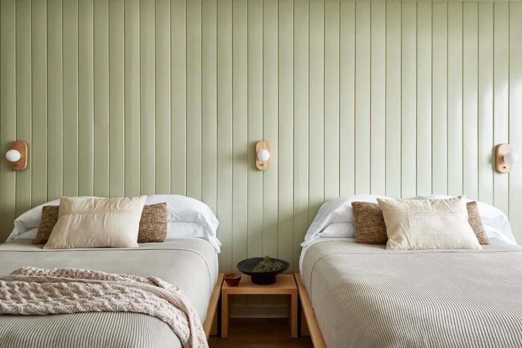 A room with two beds, a small table with a plant, and wall-mounted light fixtures.