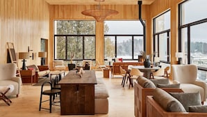 A spacious room with wooden walls, large windows, a central wooden table, and multiple seating areas. - King Jr | Laurel | Mirror Lake, Olympic History, Adirondack Adventures (Essex County)