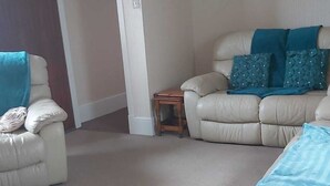 En stue med en beige sofa, en mindre lænestol og et lille træsidebord.