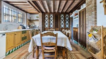 Cocina tradicional con vigas de madera, una mesa de comedor para cuatro personas y un amplio ventanal con barrotes.